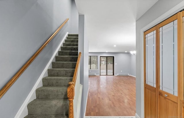 staircase featuring a baseboard heating unit, baseboard heating, wood finished floors, and baseboards