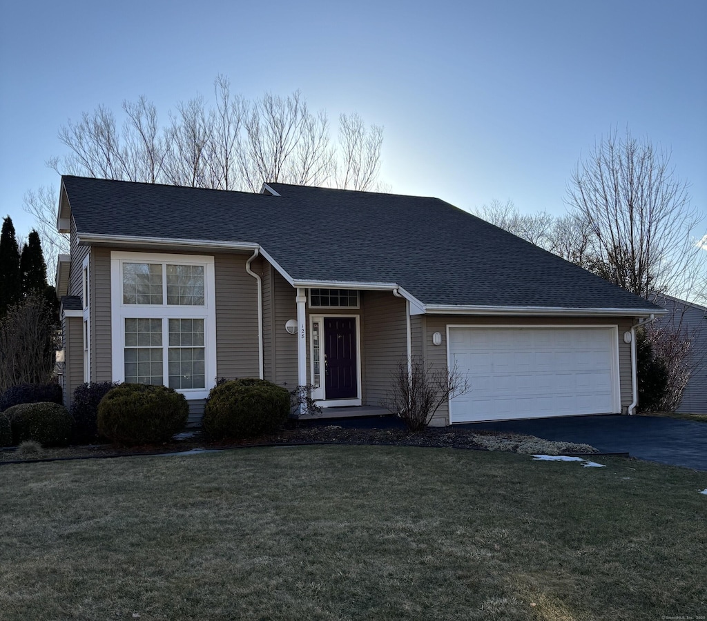 ranch-style house with an attached garage, a front lawn, aphalt driveway, and roof with shingles