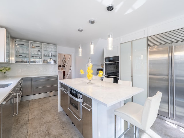 157 N Ave, Westport, CT 06880 - kitchen with a kitchen island, a breakfast bar, glass insert cabinets, appliances with stainless steel finishes, and tasteful backsplash