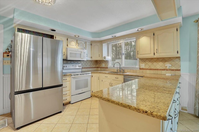 kitchen with light stone counters, light tile patterned floors, a sink, white appliances, and a peninsula