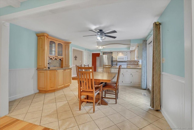 dining room with ceiling fan, light tile patterned flooring, and wainscoting