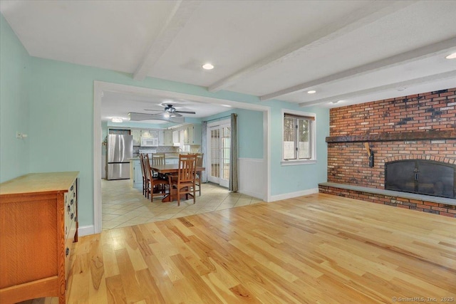 interior space with ceiling fan, beam ceiling, a fireplace, and light wood-style flooring