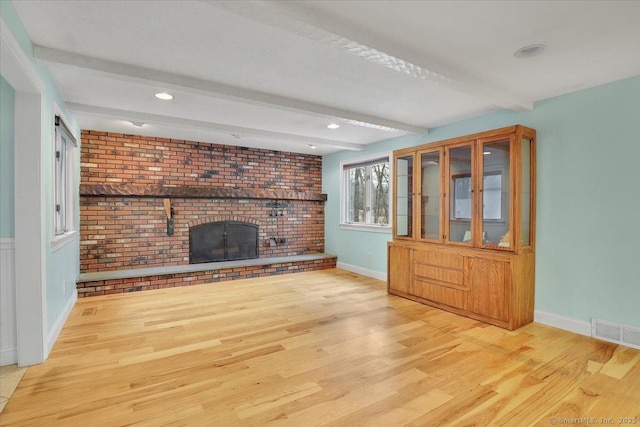 unfurnished living room featuring a brick fireplace, visible vents, wood finished floors, and beamed ceiling