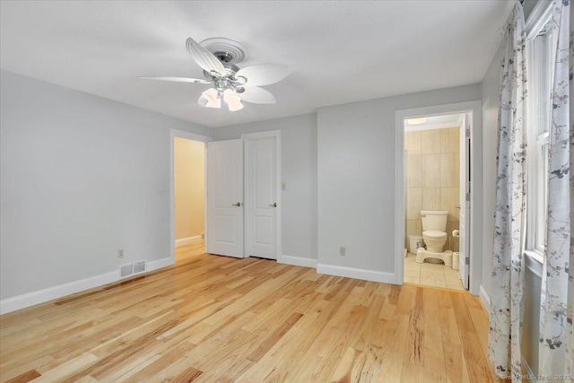 unfurnished bedroom featuring visible vents, ensuite bathroom, a ceiling fan, wood finished floors, and baseboards