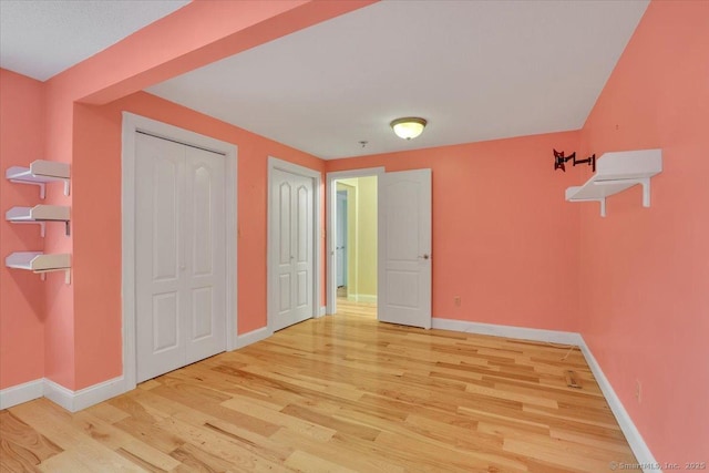 unfurnished bedroom with light wood-style floors, baseboards, and multiple closets