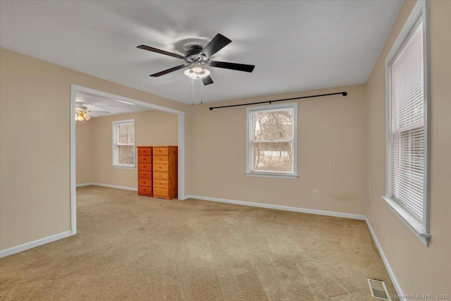 carpeted empty room featuring baseboards, a ceiling fan, visible vents, and a healthy amount of sunlight