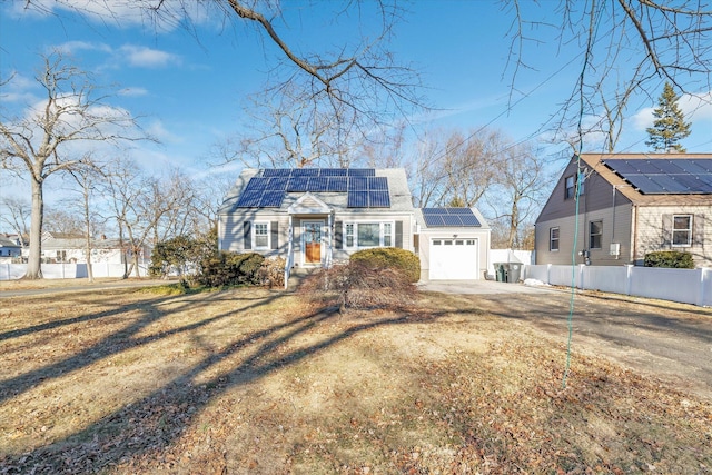 view of front of home featuring driveway, solar panels, an attached garage, fence, and a front yard