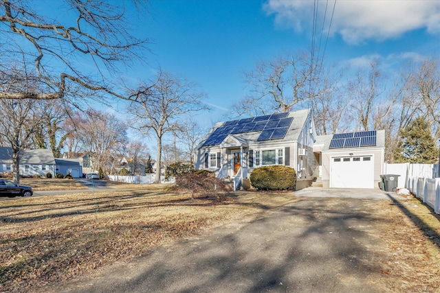 view of front of house with driveway, an attached garage, roof mounted solar panels, and fence