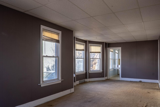 unfurnished room with carpet floors, wood walls, a paneled ceiling, and baseboards