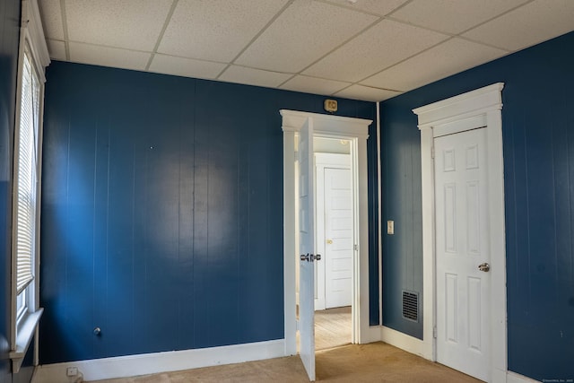 unfurnished bedroom with carpet, a drop ceiling, visible vents, and baseboards