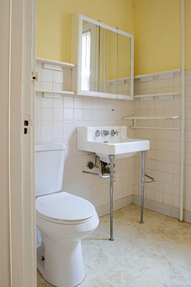 bathroom with marble finish floor, a sink, tile walls, and toilet