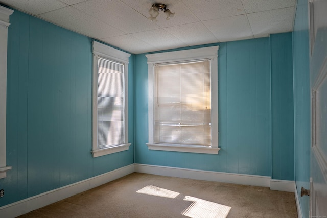 carpeted empty room with a paneled ceiling and baseboards