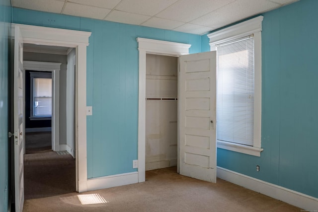 unfurnished bedroom featuring carpet floors, multiple windows, a closet, and a paneled ceiling