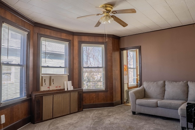 living area with carpet floors, plenty of natural light, wooden walls, and a ceiling fan