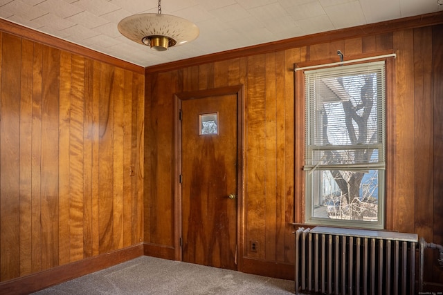 doorway to outside featuring carpet floors, radiator heating unit, and wooden walls