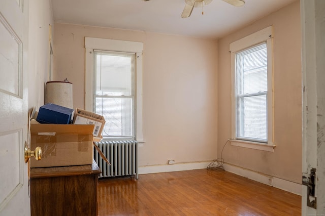 unfurnished room with radiator, ceiling fan, baseboards, and wood finished floors