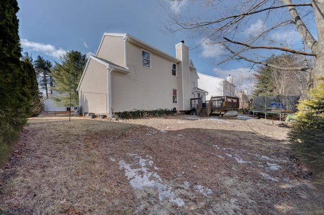 view of side of home with a trampoline, a chimney, and a wooden deck