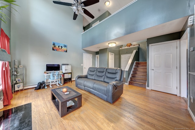 living area featuring a high ceiling, ceiling fan, wood finished floors, baseboards, and stairs