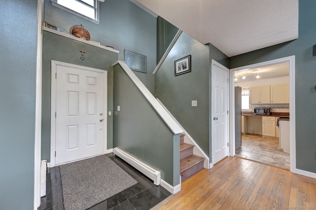 foyer featuring a textured ceiling, baseboards, light wood-style floors, stairway, and baseboard heating