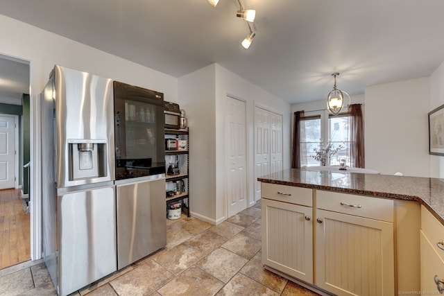 kitchen with baseboards, hanging light fixtures, stainless steel fridge with ice dispenser, dark stone countertops, and stone tile flooring