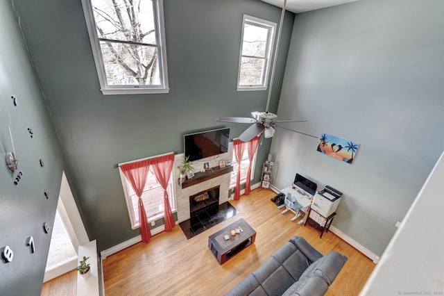 living area with a fireplace with flush hearth, ceiling fan, baseboards, and wood finished floors