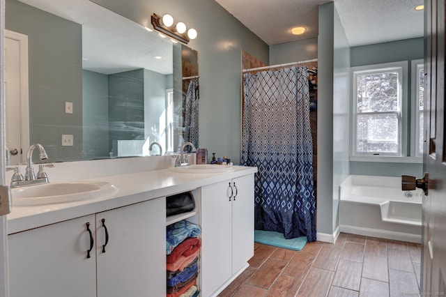 bathroom featuring a sink, a textured ceiling, a bath, and double vanity