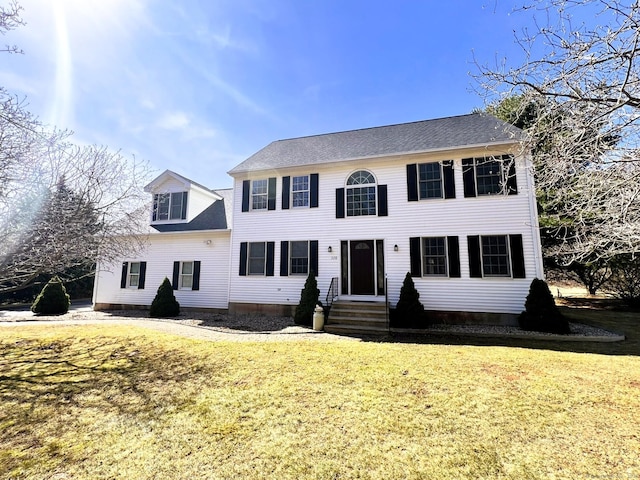 colonial house with roof with shingles, a front yard, and entry steps