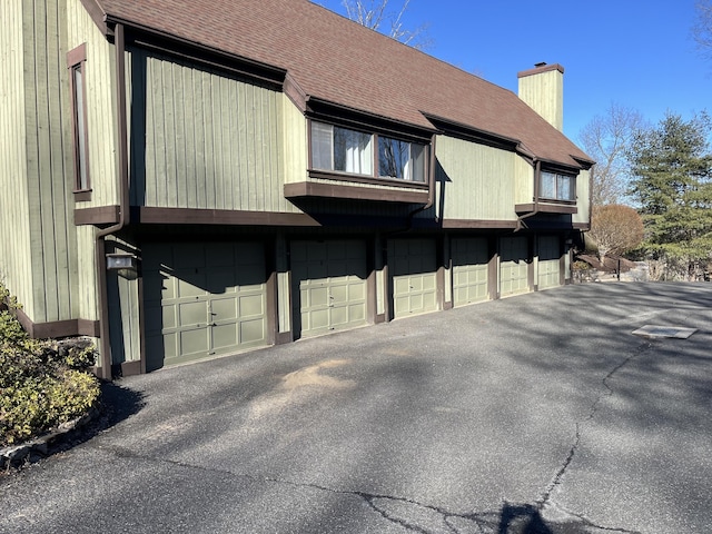 view of property exterior featuring a shingled roof, a chimney, and community garages