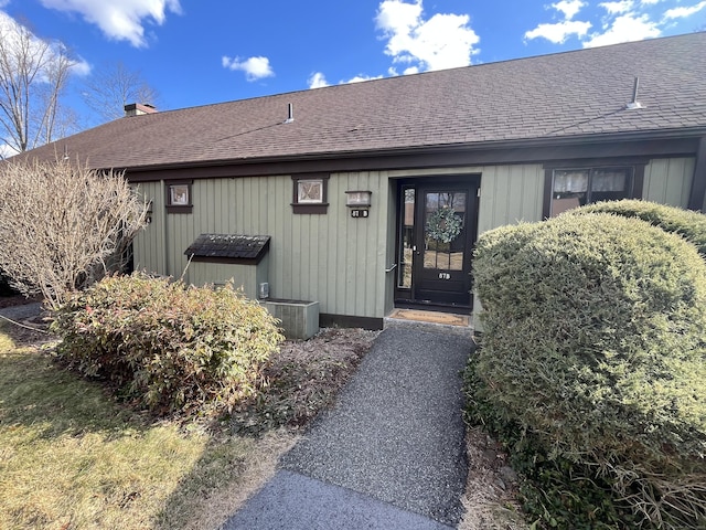 view of exterior entry featuring cooling unit and roof with shingles