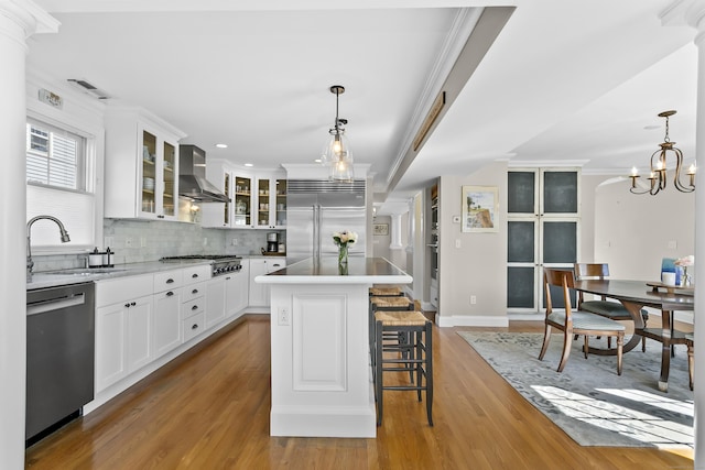 kitchen featuring stainless steel appliances, wood finished floors, a sink, wall chimney range hood, and tasteful backsplash