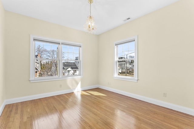 unfurnished room with a wealth of natural light, baseboards, visible vents, and hardwood / wood-style floors