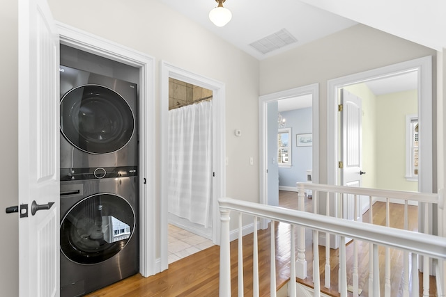 washroom featuring laundry area, wood finished floors, visible vents, baseboards, and stacked washing maching and dryer