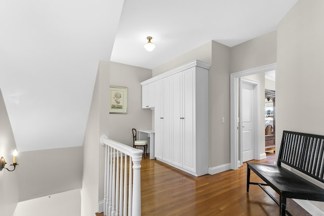 hall featuring baseboards, wood finished floors, and an upstairs landing