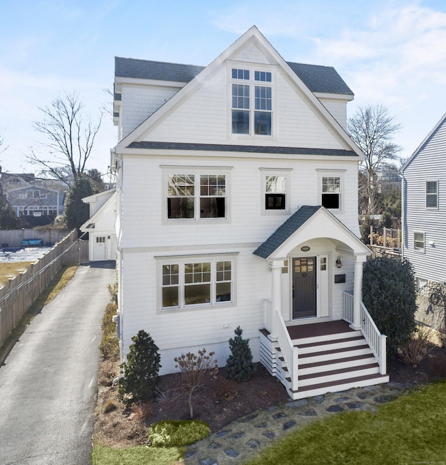 view of front facade with a garage, a shingled roof, and fence