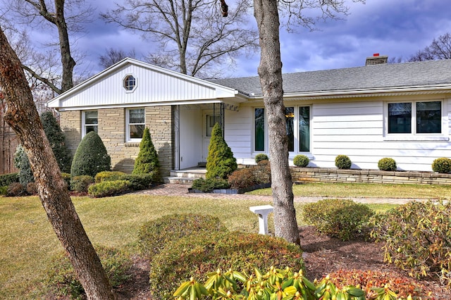 view of front facade featuring stone siding, a chimney, a front yard, and roof with shingles