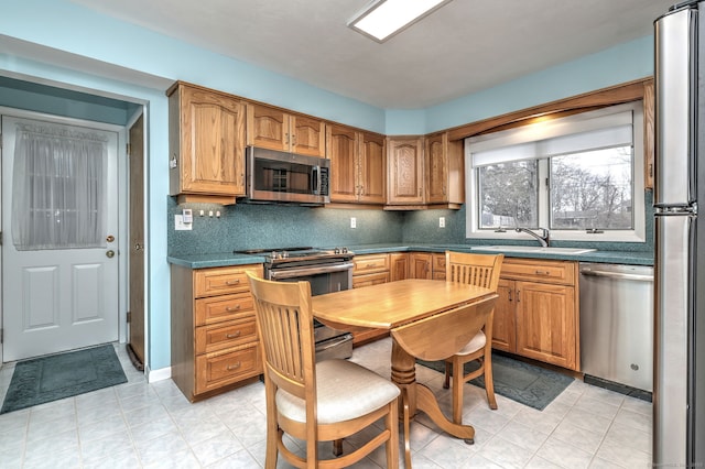 kitchen with a sink, dark countertops, backsplash, appliances with stainless steel finishes, and brown cabinetry