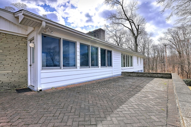 view of side of property with a patio, brick siding, and a chimney