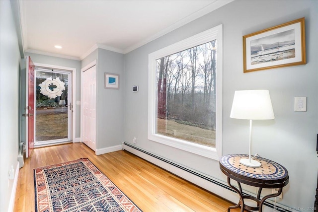 entryway with a baseboard heating unit, crown molding, baseboards, and light wood-type flooring