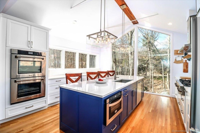 kitchen with light wood-style flooring, a sink, light countertops, appliances with stainless steel finishes, and blue cabinets