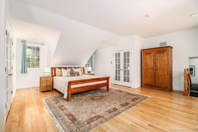 bedroom featuring light wood finished floors, visible vents, baseboards, vaulted ceiling, and french doors