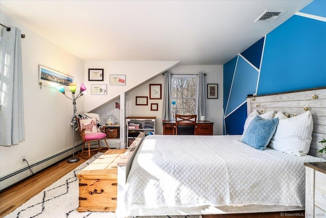 bedroom with a baseboard heating unit, wood finished floors, and visible vents