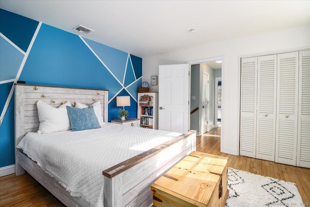 bedroom with wood finished floors, visible vents, a closet, and baseboards