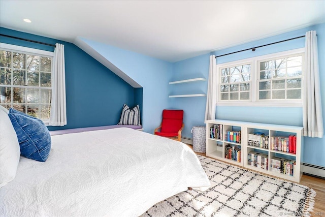 bedroom with multiple windows, baseboard heating, lofted ceiling, and wood finished floors