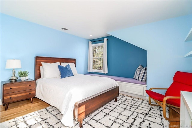 bedroom with lofted ceiling, light wood-style flooring, and visible vents