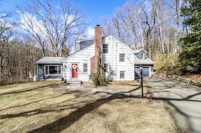 view of front of property with entry steps, aphalt driveway, a front lawn, and a chimney