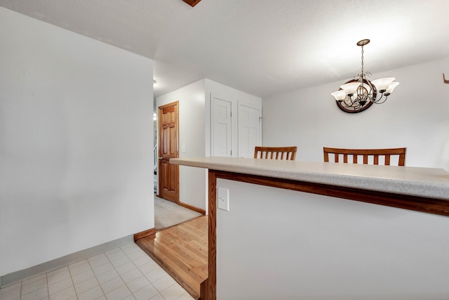 kitchen with light tile patterned floors, baseboards, an inviting chandelier, light countertops, and pendant lighting