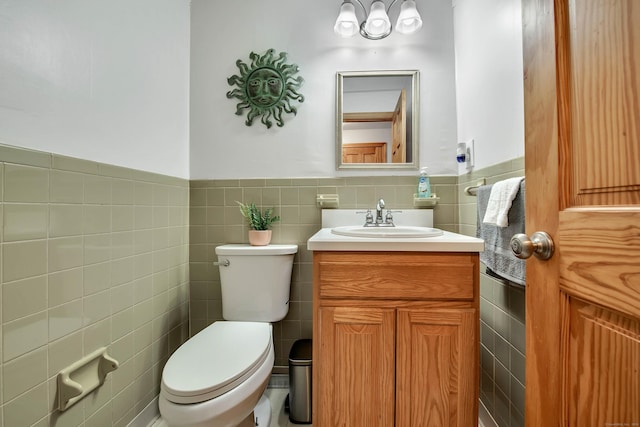 half bathroom with toilet, tile walls, wainscoting, and vanity