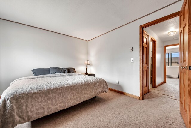 bedroom with a baseboard heating unit, baseboards, light colored carpet, and ornamental molding