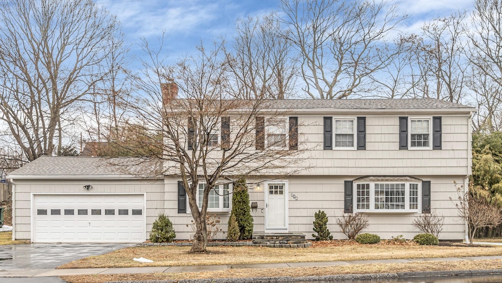 colonial home with aphalt driveway, roof with shingles, a chimney, and an attached garage