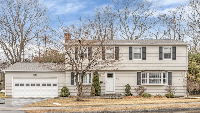 colonial home with aphalt driveway, roof with shingles, a chimney, and an attached garage